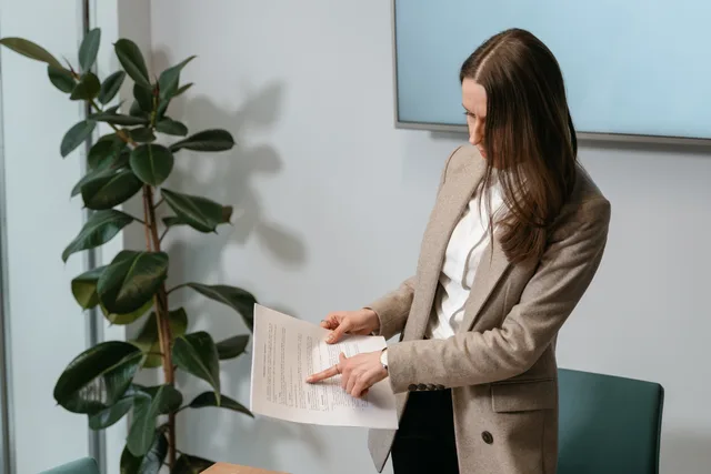 Professional woman in a brown blazer reviewing a document in an office setting. Tygodniowy przegląd rynku: jak przygotować briefing dla decydentów